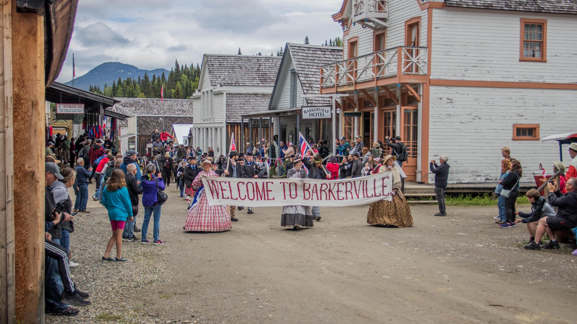 Costumed people parade through Barkerville with a sign that reads "welcome to Barkerville"