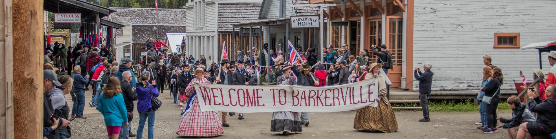 Costumed people parade through Barkerville with a sign that reads "welcome to Barkerville"
