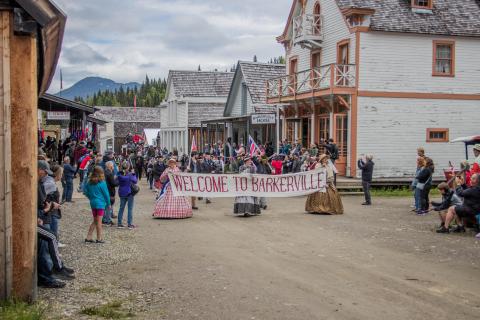 Costumed people parade through Barkerville with a sign that reads "welcome to Barkerville"